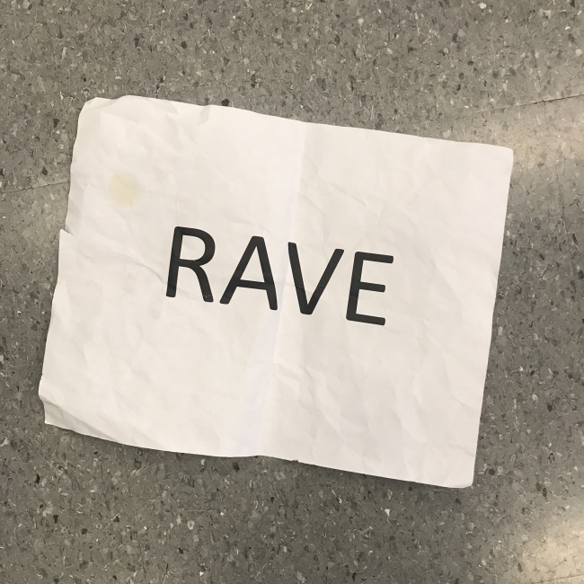 The word "RAVE" is capitalized in black lettering on a wrinkled white piece of paper and placed against a speckled grey background.