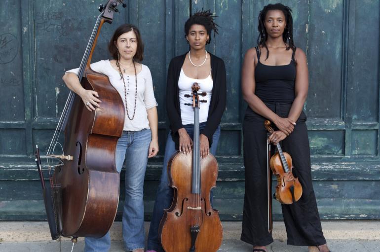 HEAR in NOW trio standing in front of a teal wall with bass, cello, and violin