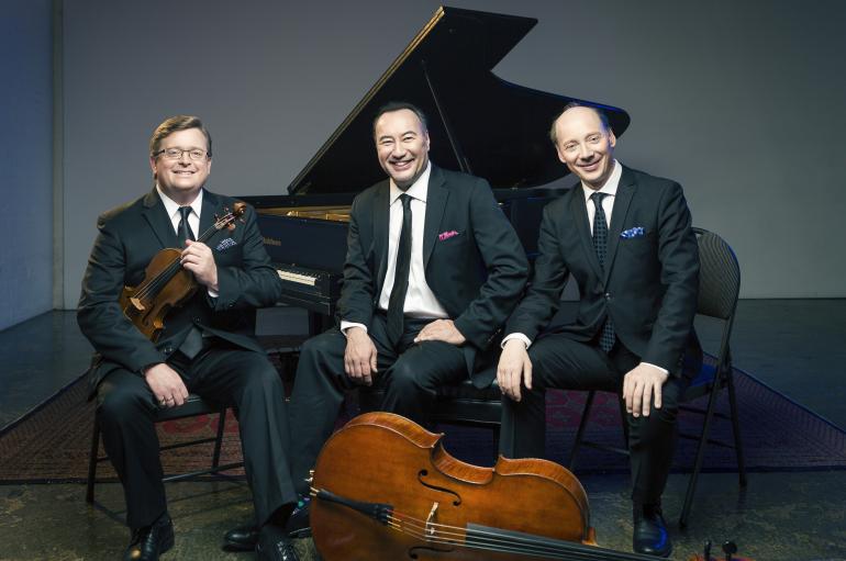 The Montrose Trio sitting with instruments in front of a piano