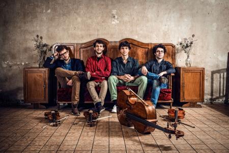 Vision String Quartet sitting on a vintage sofa with instruments in front of them