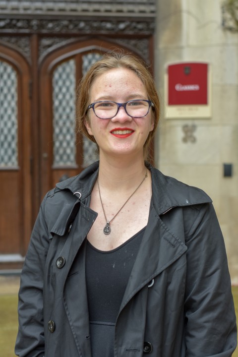 A female student poses in a black coat outside of an academic building.