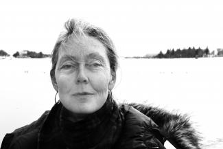 Anne Carson in a jacket by water.
