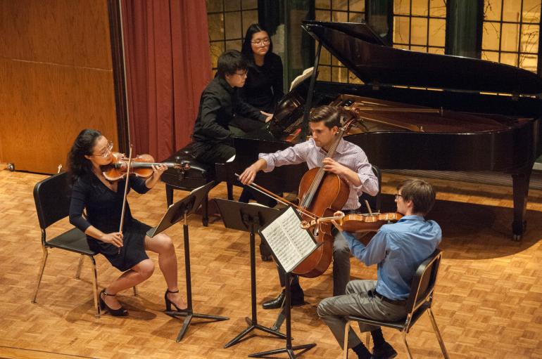 Four students, a violin, viola, and cello player and pianist, are seen from above performing on the Fulton Recital Hall stage