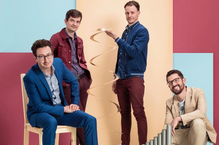 Third Coast Percussion with percussion instruments standing and sitting in front of a colorful wall