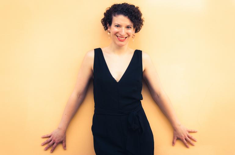 Clare Longendyke wearing a black dress standing in front of a yellow wall