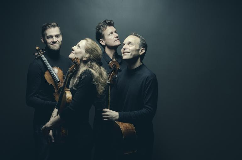 St. Lawrence String Quartet lit from above, wearing black, and holding instruments