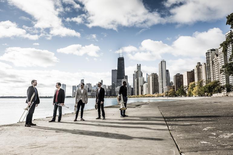 Axiom Brass standing with instruments outside, with the Chicago skyline in the background