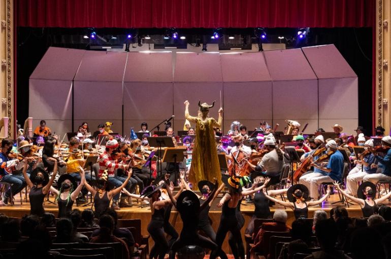 Orchestra on stage with conductor, dancers in costumes