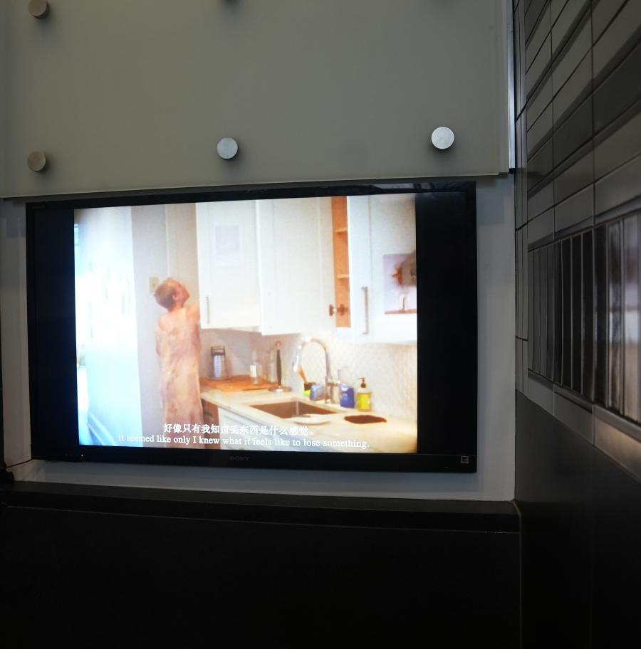 Film still of figure wearing dress in kitchen with cabinet doors open